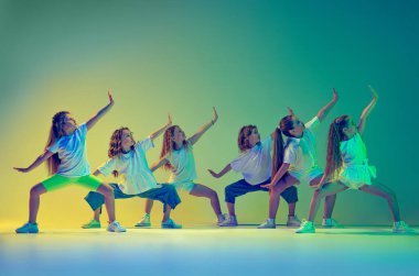 Senkronize hareketler. Bir grup çocuk, koreografi dersinde dans eden spor kıyafetleri içindeki küçük kızlar neon ışıkta yeşil arka planda izole edilmiş. Müzik, moda, sanat kavramı