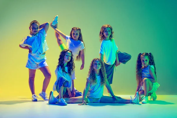 Future contemp dancers. Group of children, little girls in sportive casual style clothes dancing in choreography class isolated on green background in neon light. Concept of music, fashion, art