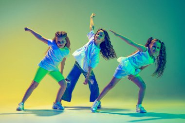 Hip-hop dansı, sokak tarzı. Bir grup çocuk, koreografi dersinde dans eden spor kıyafetleri içindeki küçük kızlar neon ışıkta yeşil arka planda izole edilmiş. Müzik, moda, sanat kavramı