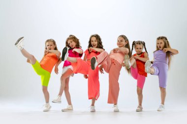 Modern koreografi dersi. Beyaz stüdyo arka planında izole halde dans eden parlak renkli elbiseli, mutlu ve aktif küçük kızlardan oluşan bir dans grubu. Müzik, moda, sanat, çocukluk, hobi kavramı.