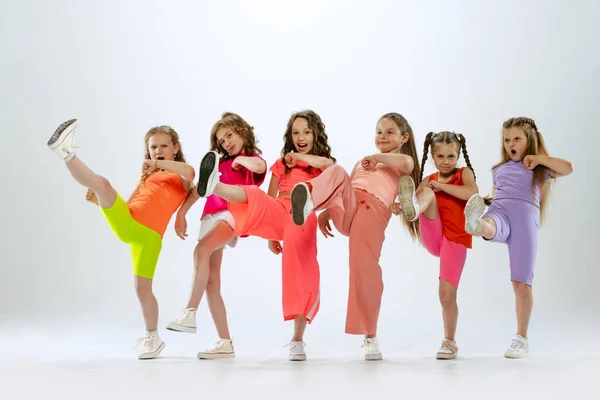 Modern choreography lesson. Dance group of happy, active little girls in bright colorful clothes dancing isolated on white studio background. Concept of music, fashion, art, childhood, hobby.