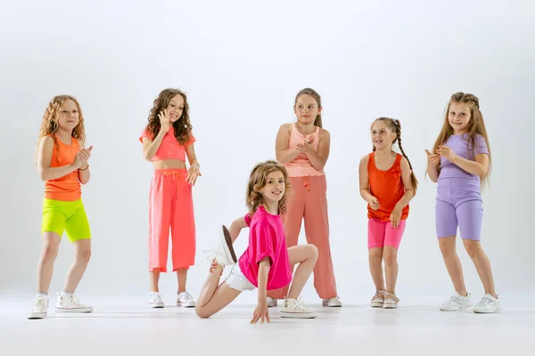 Modern choreography lesson. Dance group of happy, active little girls in bright colorful clothes dancing isolated on white studio background. Concept of music, fashion, art, childhood, hobby.