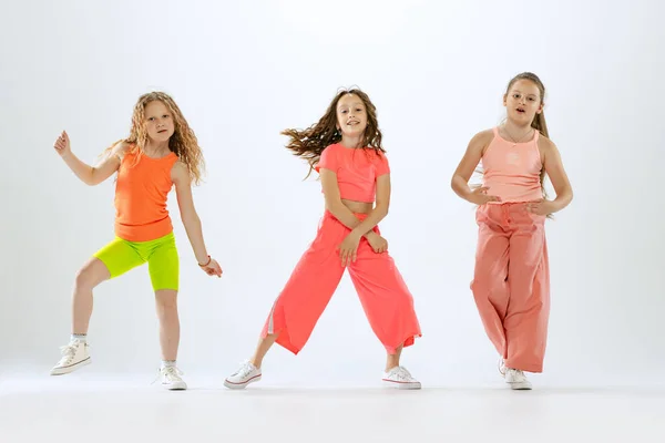 Joy, fun and happiness. Portrait of happy, active little girls, happy kids in bright colorful clothes dancing isolated on white studio background. Concept of music, fashion, art, childhood, hobby.
