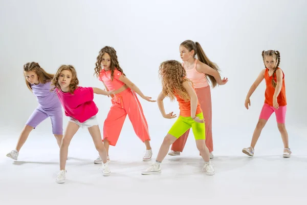 Modern choreography lesson. Dance group of happy, active little girls in bright colorful clothes dancing isolated on white studio background. Concept of music, fashion, art, childhood, hobby.