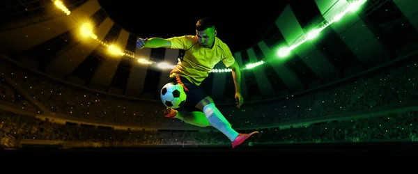 夕方の懐中電灯で混雑したスタジアムでサッカーボールでジャンプする精力的なプロサッカー選手 スポーツ 克服の概念 フィールドプレゼンス効果 — ストック写真