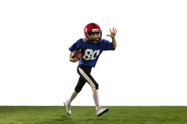 Antrenman yapıyorum. Spor üniformalı ve ekipmanlı Amerikan futbolu oynayan küçük bir çocuk yeşil çimen zeminli beyaz arka planda izole edilmiş. Spor, reklam, hareket, başarı kavramı.