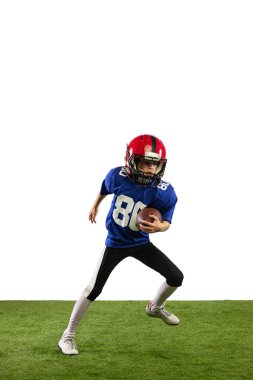 Antrenman yapıyorum. Spor üniformalı ve ekipmanlı Amerikan futbolu oynayan küçük bir çocuk yeşil çimen zeminli beyaz arka planda izole edilmiş. Spor, reklam, hareket, başarı kavramı.