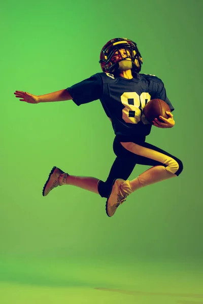 飞啊穿着运动服和装备的活泼小男孩在霓虹灯下被隔离在绿色背景下踢足球 成就的概念 — 图库照片