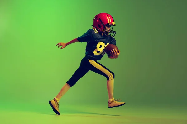 前に進む ネオンの光の中で緑の背景に隔離されたアメリカのサッカーを再生するスポーツの制服や機器のスポーツ少年 スポーツ 成果の概念 — ストック写真