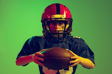 Oyuna hazırlan ve kazan. Duygusal çocuğun yakın plan portresi, spor üniformalı Amerikan futbolcusu ve neon ışıkta yeşil arka planda izole edilmiş kask. Spor anlayışı, meydan okumalar