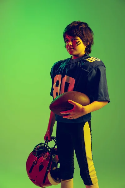 1人のスポーツ少年 青いスポーツのユニフォームを着たアメリカのサッカー選手とネオンの光の中で緑の背景に隔離されたポーズ保護装置 スポーツ 成果の概念 — ストック写真