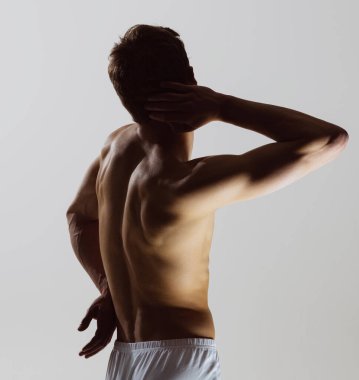 Model siluet. Gri arka planda tek başına duran beyaz boxer külotlu genç, üstsüz, kaslı bir adam. Sağlık, refah, fitness, spor konsepti. Erkek vücudunun doğal güzelliği