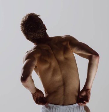 Model siluet. Gri arka planda tek başına duran beyaz boxer külotlu genç, üstsüz, kaslı bir adam. Sağlık, refah, fitness, spor konsepti. Erkek vücudunun doğal güzelliği