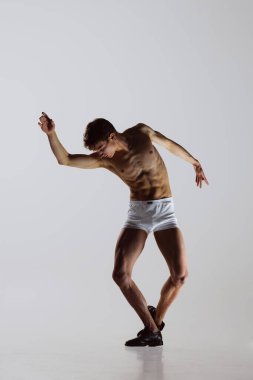 Modern, düşünceli. Genç sanatçı, esnek erkek dansçı gri stüdyo arka planında izole edilmiş. Sanat, hareket, esneklik, ilham konsepti. Esnek bir sanatçı. Erkek vücudunun güzelliği