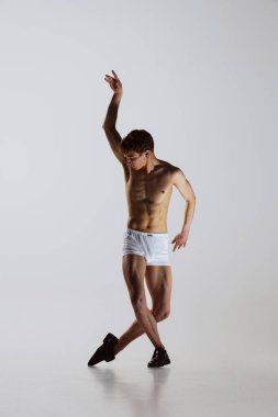 Modern, düşünceli. Genç sanatçı, esnek erkek dansçı gri stüdyo arka planında izole edilmiş. Sanat, hareket, esneklik, ilham konsepti. Esnek bir sanatçı. Erkek vücudunun güzelliği