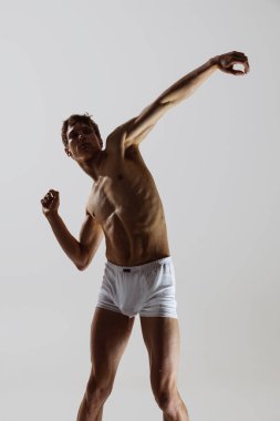 Umut. Duygularını hareketlerle ifade et. Düşünce dansı, performans. Gri arka planda yalnız dans eden, iç çamaşırlı, esnek, genç bir adam. Sanat, müzik, güzellik. Sağlıklı yaşam tarzı kavramı