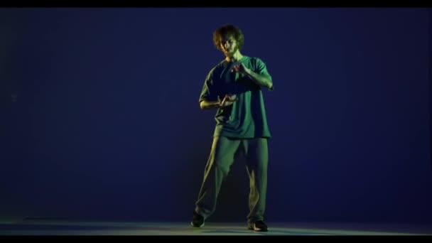ストリートダンス スタイリッシュな若者 ネオンの光の中で濃い青の背景に隔離されたスポーツカジュアルスタイルの衣装を身に着けているヒップホップダンサー モダンダンスアート ファッション スタイルのコンセプト ビデオ — ストック動画
