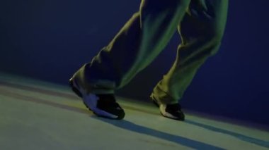Sallanıyor. Erkek bacakları, hip-hop dansçıları, neon ışıkta koyu mavi arka planda zıplıyorlar. Modern dans sanatı, moda, gençlik, reklam, tarz konsepti. 4K, video