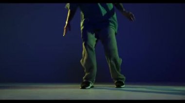 Step dansı. Erkek bacaklar, hip-hop dansçısı koyu mavi arka planda, neon ışıkta izole edilmiş. Modern dans sanatı, moda, gençlik, reklam, tarz konsepti. 4K, video