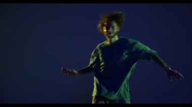 Güçlü hareketler. Neşeli genç bir adam, hip-hop dansçısı koyu mavi arka planda izole edilmiş neon ışıkta dans ediyor. Modern dans sanatı, moda, gençlik, reklam, tarz konsepti. 4K, video