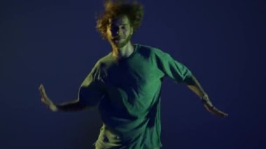 El salla. Neşeli genç bir adam, hip-hop dansçısı koyu mavi arka planda izole edilmiş neon ışıkta dans ediyor. Modern dans sanatı, moda, gençlik, reklam, tarz konsepti. 4K, video