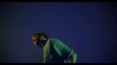 Heyecanlı genç adam, hip-hop dansçısı koyu mavi arka planda izole edilmiş neon ışıkta dans ediyor. Modern dans sanatı, moda, gençlik, reklam, tarz konsepti. 4K, video. Model