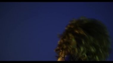 Kafasını sallayan kıllı genç adamın arka görüntüsü koyu mavi arka planda, neon ışıkta izole edilmiş. Modern dans sanatı, moda, gençlik, reklam, tarz konsepti. 4K, video. Yakın plan.