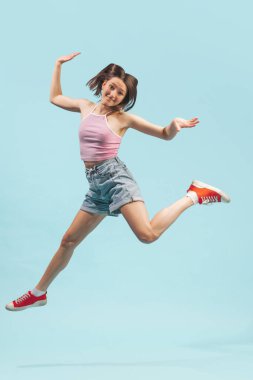 Mutluluk. Mavi arka planda tek başına atlayan bluz ve kot şort giyen mutlu bir kız. Duyguların kavramı, yüz ifadesi, gençlik, arzu, satış