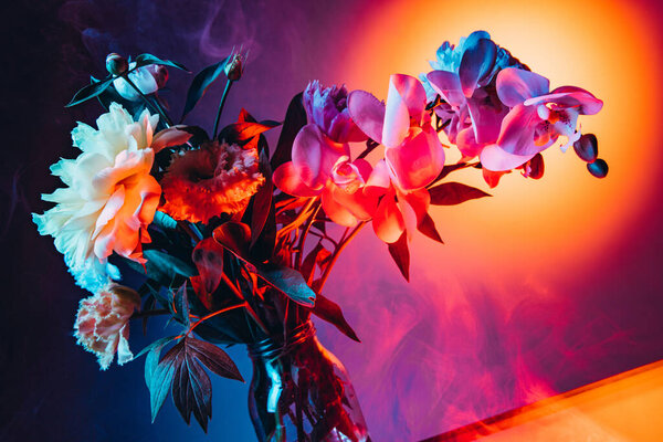 Urban sunset. Live flowers, creative floral composition over purple-yellow background in neon light. Concept of floristry, decorations, creativity, decor and ad. Design for wallpaper