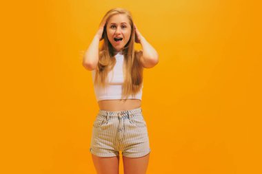 Vay canına, bağırıyor. Sarı arka planda izole edilmiş beyaz tişört giyen uzun sarı saçlı afallamış genç bir kız. İnsan duyguları kavramı, yüz ifadesi, gençlik, arzu, reklam