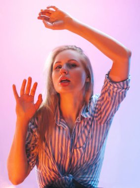 Yakın plan genç kız neon ışıklarıyla izole edilmiş pembe stüdyoda cama çarpmış. İnsan duyguları, yüz ifadesi, gençlik kavramı. Cama yaslanmış bir model