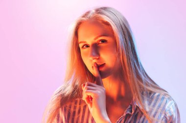 - Gizli. Genç, güzel bir kız, uzun sarı saçlı bir öğrenci pembe arka plandaki neon ışıkta izole edilmiş kameraya bakıyor. İnsan duyguları kavramı, yüz ifadesi, gençlik, arzu, reklam