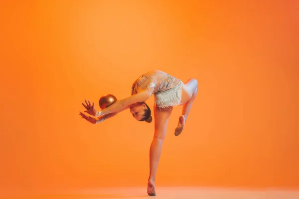 優雅な動きだ オレンジ色の背景に隔離された金色のボールを持つ1つのプロのリズミカルな体操アーティストのトレーニング スポーツ アクション アクティブライフスタイルの概念 — ストック写真