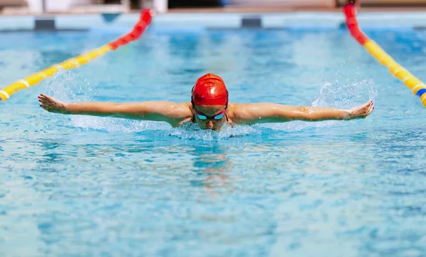 Butterfly swimming technique. Live portrait of young woman, swimmer in swimming cap and goggles practicing at public swimming-pool, outdoors. Sport, power, energy, style, hobby concept.