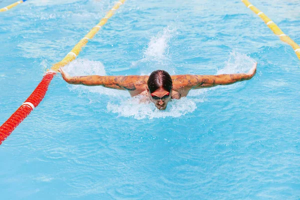 Butterfly swimming technique. Young muscular man, professional swimmer in goggles training at public swimming-pool, outdoors. Sport, power, energy, style, hobby concept. Celestial blue water