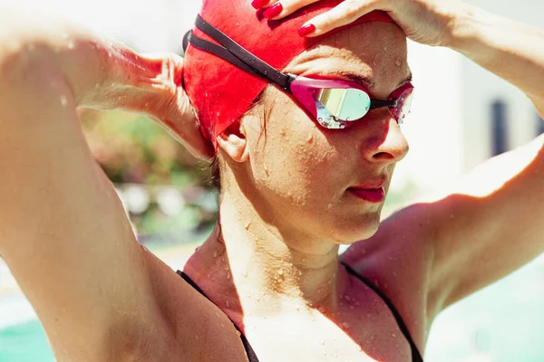 Champion. Sportive woman swimmer in red cap and googles getting ready to start of swim at open public pool, outdoors. Vacation, active lifestyle, power, energy, sports movement concept.