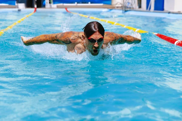 Butterfly swimming technique. Young muscular man, professional swimmer in goggles training at public swimming-pool, outdoors. Sport, power, energy, style, hobby concept. Celestial blue water