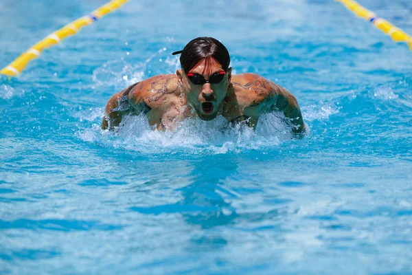 Butterfly swimming technique. Young muscular man, professional swimmer in goggles training at public swimming-pool, outdoors. Sport, power, energy, style, hobby concept. Celestial blue water