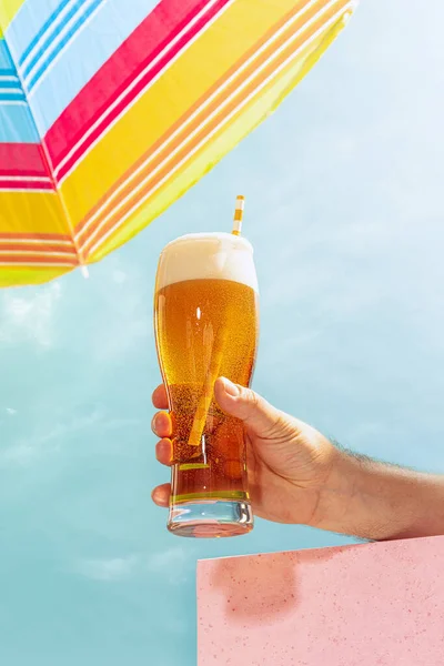 Bright hot day and cold drinks. Human hand holding glass of cold light beer over summer blue sky background. Vacation, happiness, drinks, beach, travel, fest and ad concept. Retro style.