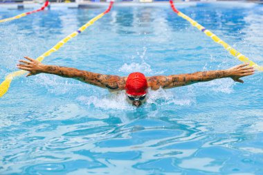 Kelebek yüzme tekniği. Genç kaslı adam, gözlüklü profesyonel yüzücü halka açık yüzme havuzunda eğitim görüyor. Spor, güç, enerji, tarz, hobi konsepti. Göksel mavi su