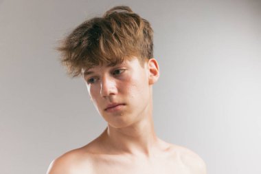 Utangaçlık. Gri stüdyo arka planında izole edilmiş genç bir adamın güzel portresi. Genç cilt bakımı, sağlık, sorunlu cilt için kozmetik, gençlik kavramı. Sanat, moda, sağlıklı yaşam tarzı ve reklam.