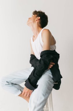 Beyaz stüdyo arka planında izole edilmiş yakışıklı erkek portresi. Moda anlayışı, gençlik, duygular, yüz ifadesi, reklam. Moda erkek modelleri gündelik kıyafetlerle poz veriyor. Sakin, ciddi görünüyor.