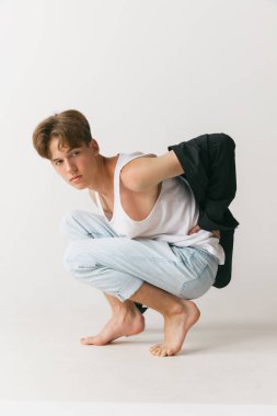 Beyaz stüdyo arka planında izole edilmiş yakışıklı erkek portresi. Moda anlayışı, gençlik, duygular, yüz ifadesi, reklam. Moda erkek modelleri gündelik kıyafetlerle poz veriyor. Sakin, ciddi görünüyor.