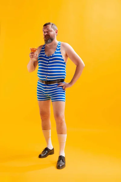 칵테일을 재미있는 남자가 역줄무늬 수영복을 노란색 배경에서 고립된 포즈를 취하고 — 스톡 사진