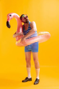 Rüyamda denizi gördüm. Sarı arka planda izole edilmiş komik şişman sakallı, çizgili mayo giymiş komik bir adam portresi. Yaz, sahil, dinlenme ve eğlence zamanı konsepti.