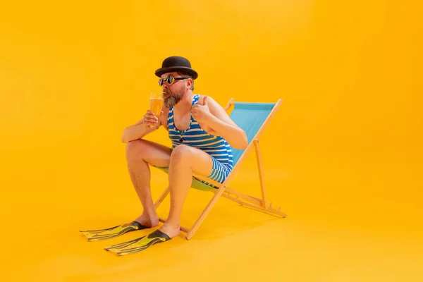 ビールを飲む クールな面白いビーチガーのスタジオ撮影 ヴィンテージストライプの水着と黄色の背景に孤立サンベッドに座ってボウラー帽子の男 レジャー活動 — ストック写真