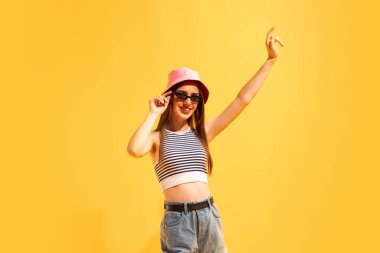 Selamlaşmak için elini sallıyor. Sarı arka planda izole edilmiş duygusal genç kızın stüdyo çekimi. Güzellik, sanat, moda, duygular, gençlik, yaz modası, tatil kavramı. İlan için alanı kopyala