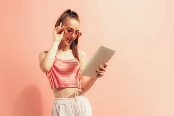 Looking at device screen. One young charming girl using digital tablet isolated on peach color background. Concept of beauty, art, fashion, emotions, youth. Copy space for ad