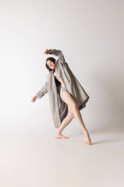 Mutluluk. Gri arka planda, hareketli iç çamaşırlı ve ceketli dans eden genç bir kadın. Sanat, hareket, hareket, esneklik, ilham konsepti. İlan ve tasarım için alanı kopyala