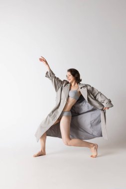 Duygular. Gri arka planda izole edilmiş iç çamaşırlı ve palto danslı genç bir kadının dinamik portresi. Sanat, hareket, hareket, esneklik, ilham konsepti. Tek kişilik performans